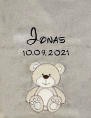 Couverture bébé grise, ultra-douillette, broderie : en haut au centre « Jonas » en lettres cursives noires, dessous date de naissance 10/09/2021. Plus bas, un ours en peluche beige aux contours marron foncé, visage souriant.