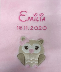 Une couverture pour bébé rose, brodée du prénom « Emilia » et de la date « 15/11/2020 » en lettres rose foncé. En dessous, une adorable chouette beige et blanche aux grands yeux, coiffée d'un petit nœud rose, est brodée.