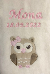 Couverture bébé beige ultra-douillette avec broderie rose : prénom « Mona » et date « 18/09/2022 ». En dessous, une application chouette marron clair, grands yeux, nez cœur rose et nœud rose. Douillette, moelleuse.